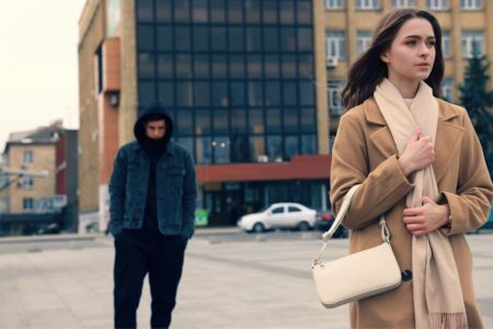a hooded man following a woman on the street