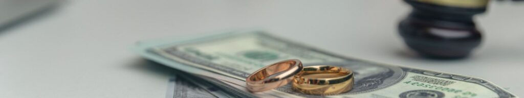 A stack of bills with wedding rings and a judge's gavel on a desk